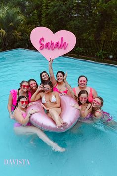 a group of women in swimsuits holding up a heart shaped sign while sitting on an inflatable raft