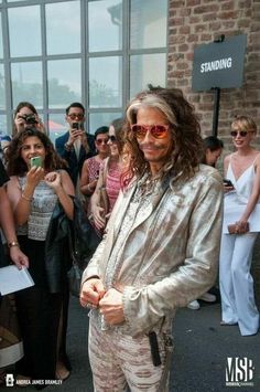 a man with long hair and sunglasses standing in front of a group of people