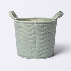 a small round basket with handles and wavy design on the sides, sitting on a white surface