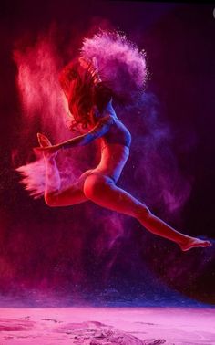 a woman is dancing in the air with colored powder on her body