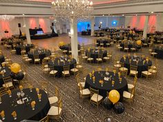 tables and chairs are set up with black tablecloths, yellow balloons, and gold rimmed centerpieces