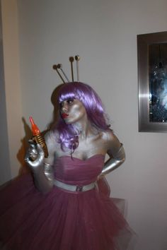 a woman with purple hair is dressed in costume and holding an orange object while standing next to a wall