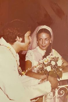 an old photo of a man and woman getting married in front of a gate with flowers