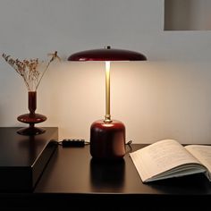 an open book on a desk next to a lamp and vase with flowers in it