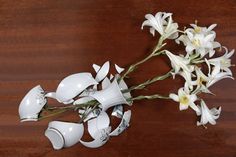 some white flowers on a wooden table with one flower in the middle and two broken vases next to it