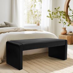 a bed with a black bench in front of it and a mirror on the wall