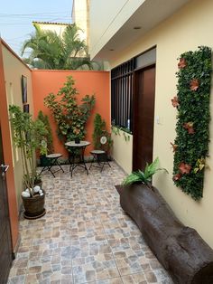 an outdoor patio with potted plants on the wall and wooden bench in between two buildings