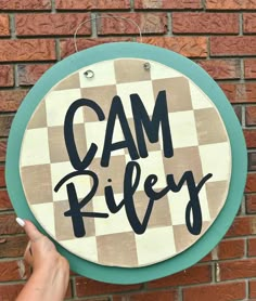 a sign that says cam riley hanging on the side of a brick wall with a hand pointing at it