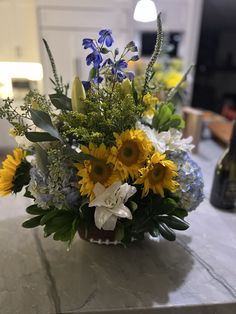 a vase filled with yellow and white flowers on top of a table next to a bottle of wine