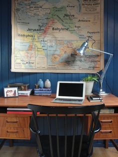 a laptop computer sitting on top of a wooden desk next to a wall mounted map