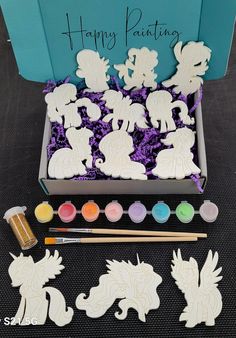 a box filled with lots of cut outs next to some paint and brushes on top of a table