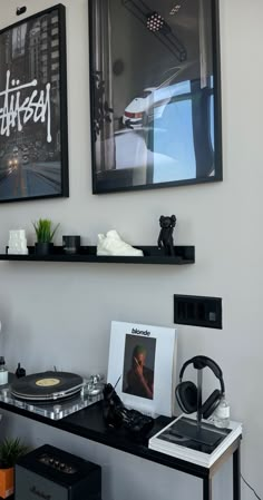 two framed pictures hang on the wall above a record player and other items in front of them