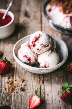 three scoops of ice cream in a bowl with strawberries on the table next to it