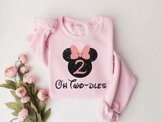 a pink sweatshirt with minnie mouse ears and the number two on it, next to flowers