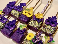 there are many purple and yellow decorated treats on the table with gold forks next to them