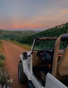 a jeep parked on the side of a dirt road next to a lush green field