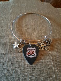 "Fun charms and a Route 66 guitar pick make up this stainless adjustable bangle bracelet. The bangle expands to slide over the hand but fits a 7\" wrist best" Adjustable Silver Jewelry For Concert, Adjustable Silver Jewelry For Concerts, Adjustable Music-themed Jewelry For Concerts, Adjustable Silver Bracelets For Concerts, Guitar Pick Bracelet, Adjustable Metal Music-themed Jewelry, Adjustable Bracelet Jewelry For Concerts, Adjustable Nickel-free Stainless Steel Bangle, Adjustable Stainless Steel Nickel-free Bangle