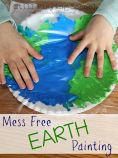 two hands on top of a paper plate that has the earth painted in green and blue