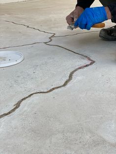 a man in blue gloves is working on a concrete floor with a hole cut into the ground