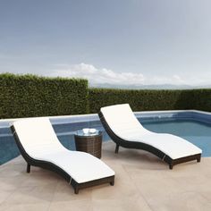 two lounge chairs next to a swimming pool in the middle of an open area with hedges