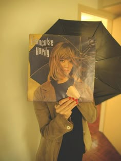 a woman holding an umbrella and magazine in front of her face while standing next to a wall