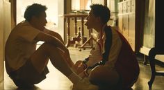 two young men sitting on the floor in front of a door talking to each other