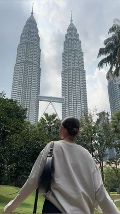 a woman is standing in front of two tall buildings with trees and bushes behind her