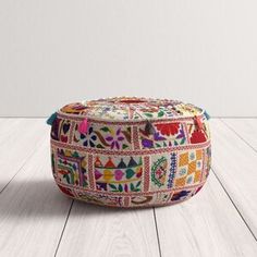 a multicolored round ottoman with tassels sits on a white wooden floor