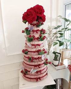 a multi - tiered cake decorated with red roses and butterflies is displayed on a table