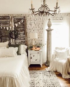 a bedroom with a bed, chandelier and pillows on the floor in front of a brick wall