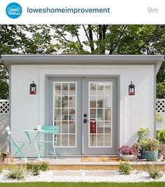 a small white shed with two doors and windows on the outside, next to a table and chairs