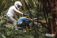 a man riding on the back of a blue motorcycle through a forest filled with trees