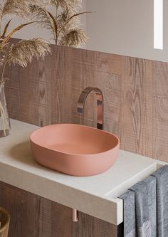 a bowl shaped sink sits on a counter next to a vase with dry grass in it