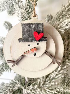 a snowman ornament with a red heart hanging from it's head