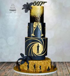 a black and gold cake with golden decorations on the top, surrounded by figurines