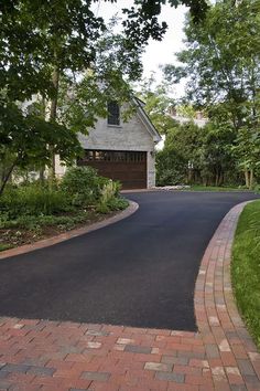 a driveway with brick pavers leading to a house in the distance and trees around it