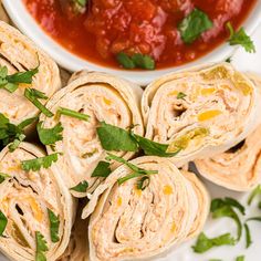 several burritos are arranged on a plate with salsa and cilantro in the background