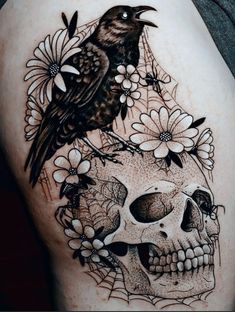 a black bird sitting on top of a human skull with flowers and leaves around it