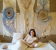 a woman sitting on top of a bed in front of two wall hangings with flowers