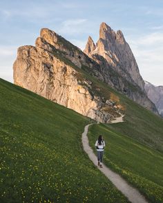 a woman is walking down a path in the mountains