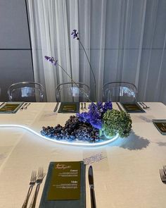 the table is set with silverware and purple flowers in a bowl on top of it