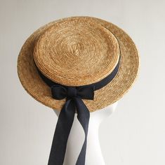 Coco Monroe Hat. Natural Milan Straw Boater Hat by And They Loved Hats. This charming and sporty hat is handcrafted in natural wheat straw. Classic and uncluttered, simply accented with long romantic trailing dark navy ribbon hatband and bow. The boater brim is perfectly flat and has a steel wired brim edge. The interior is fitted with an ribbon lining. This attention to detail and finishing adds lasting quality. The boater attaches with a discreet hair matching millinery elastic.   Casual or fo Classic Adjustable Straw Hat For Weddings, Adjustable Brimmed Boater Hat For Wedding, Beach Boater Hat With High Crown, Fitted High Crown Boater Hat For Beach, Adjustable Vintage Straw Hat For Weddings, Adjustable Wide Brim Straw Hat For Wedding, Adjustable Boater Hat For Summer Wedding, Adjustable Brimmed Sun Hat For Wedding, Adjustable High Crown Straw Hat For Kentucky Derby