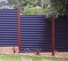 a black fence with wooden slats in the middle and plants growing on the side