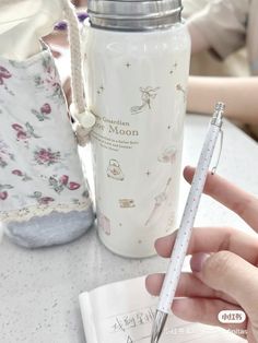 a person is holding a pen and writing on a notebook next to a water bottle