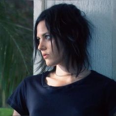 a woman with black hair is leaning against a wall