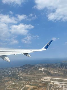 the wing of an airplane flying over land and water below it is blue with white clouds