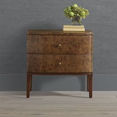 a wooden dresser with a flower pot on top and a book on the bottom, against a gray wall