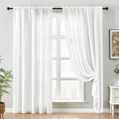 a living room with white curtains and wooden floors in front of a large window that has a potted plant next to it