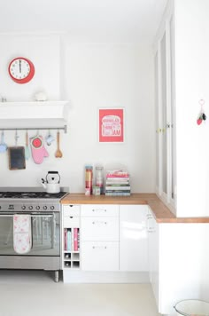 a kitchen with white cabinets and a silver stove top oven in front of a clock on the wall