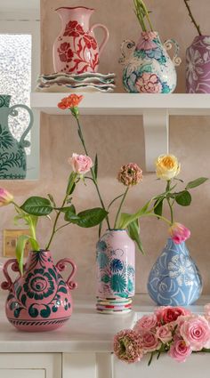 several vases with flowers in them on a shelf next to other vases and plates